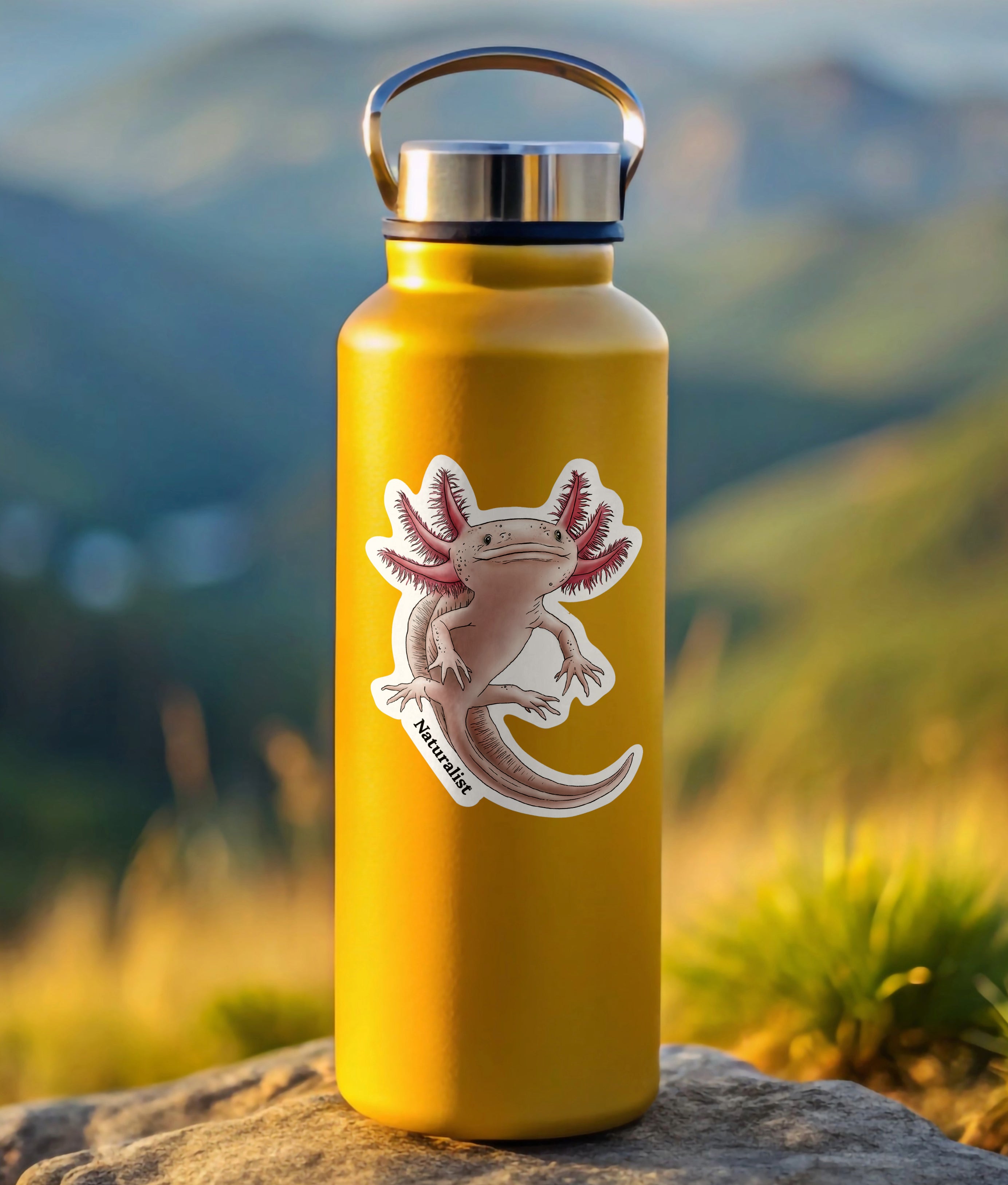 Yellow water bottle with a axolotl sticker on a rock with a mountainous background