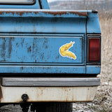 Rustic blue truck with a yellow banana slug decal in a natural setting