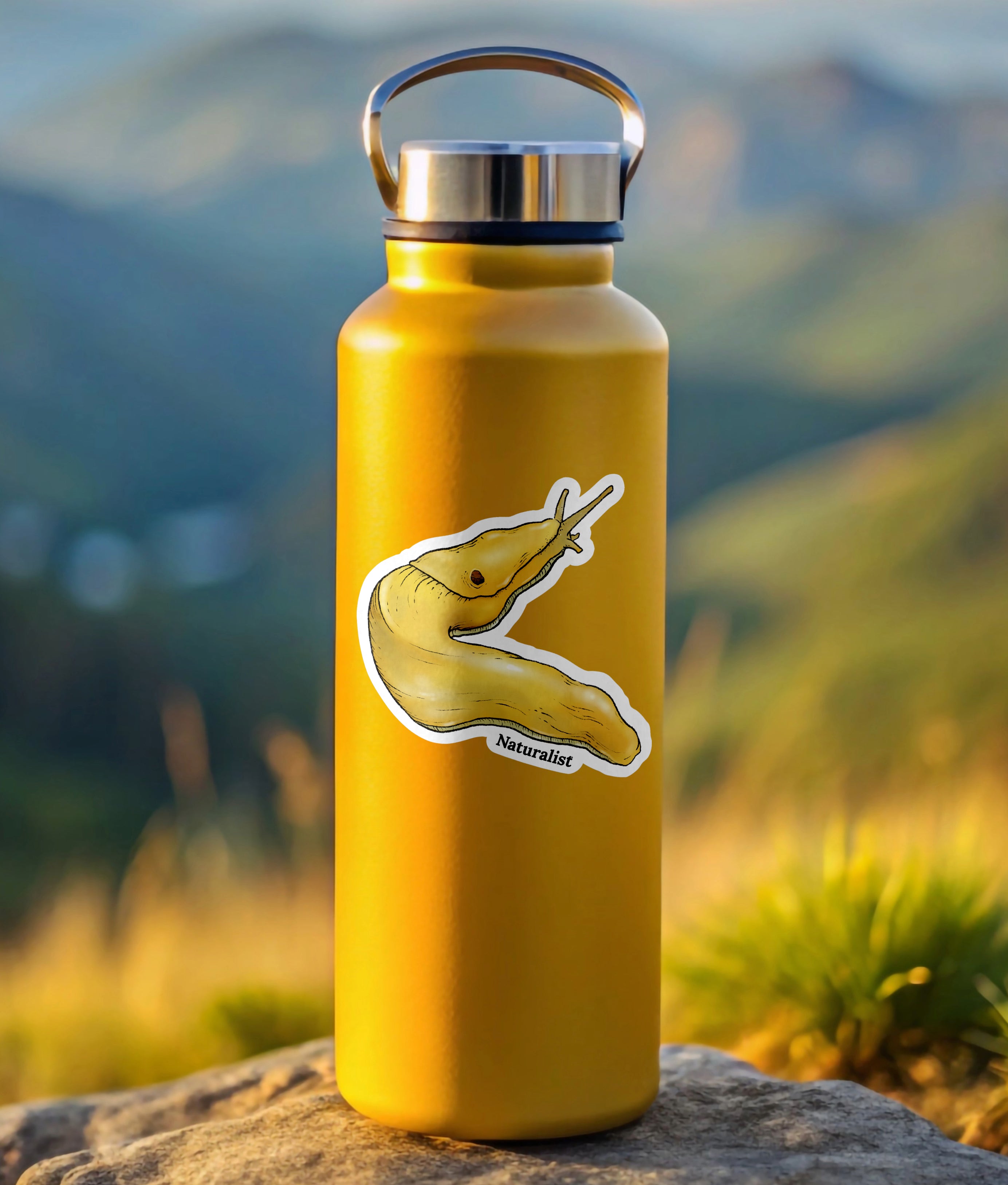 Yellow water bottle with a sticker of a banana slug on a rock with a mountainous background