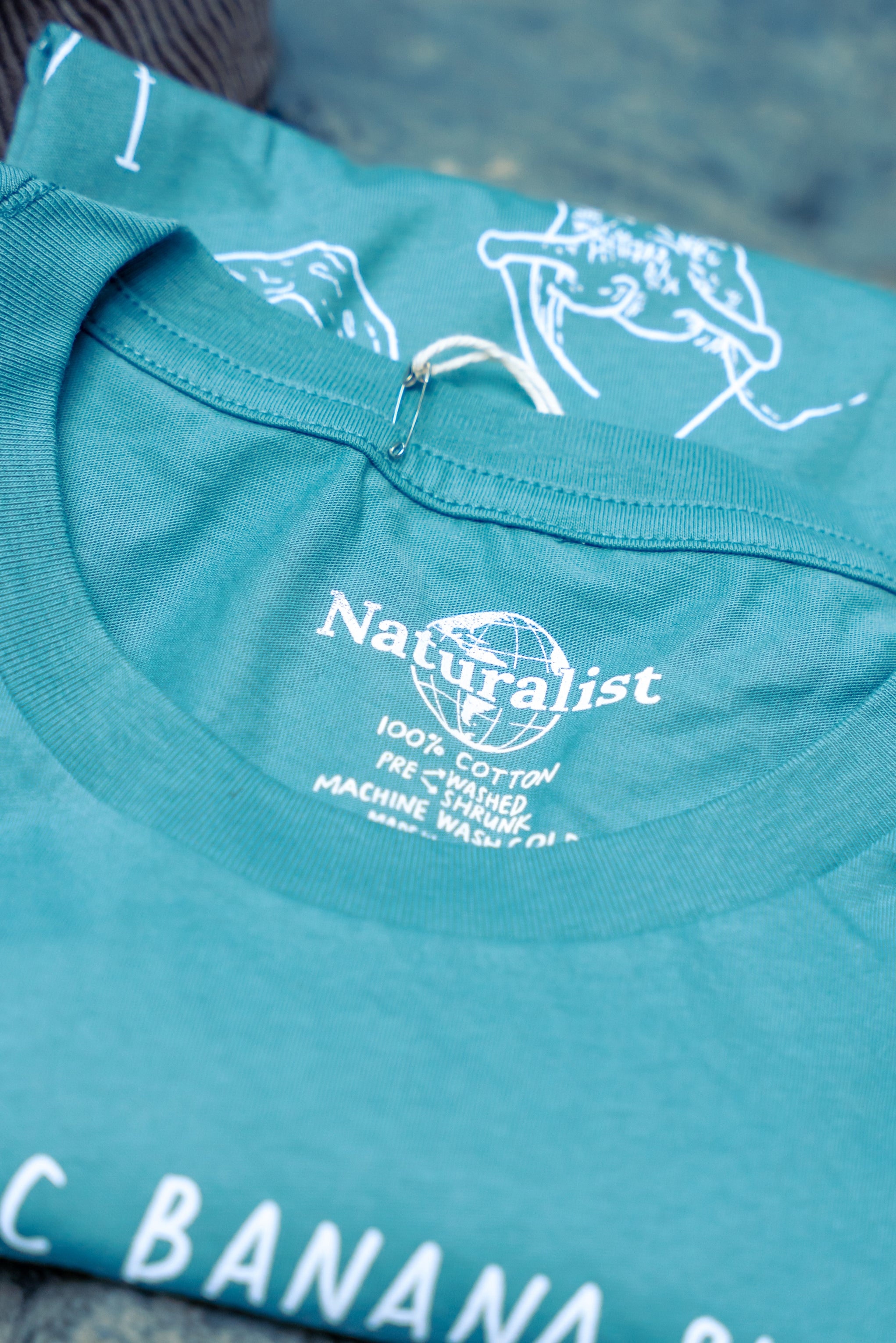 Close-up of a turquoise t-shirt with 'Naturalist' branding and text.