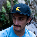 Man wearing a navy cap with a yellow banana slug in front of a waterfall