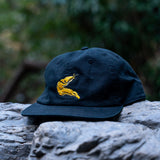 Navy blue cap with yellow banana slug design on a rock with blurred green foliage in the background