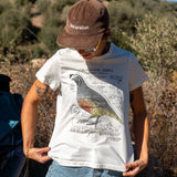 Person wearing a white t-shirt with a bird graphic and text, standing outdoors in a natural setting.