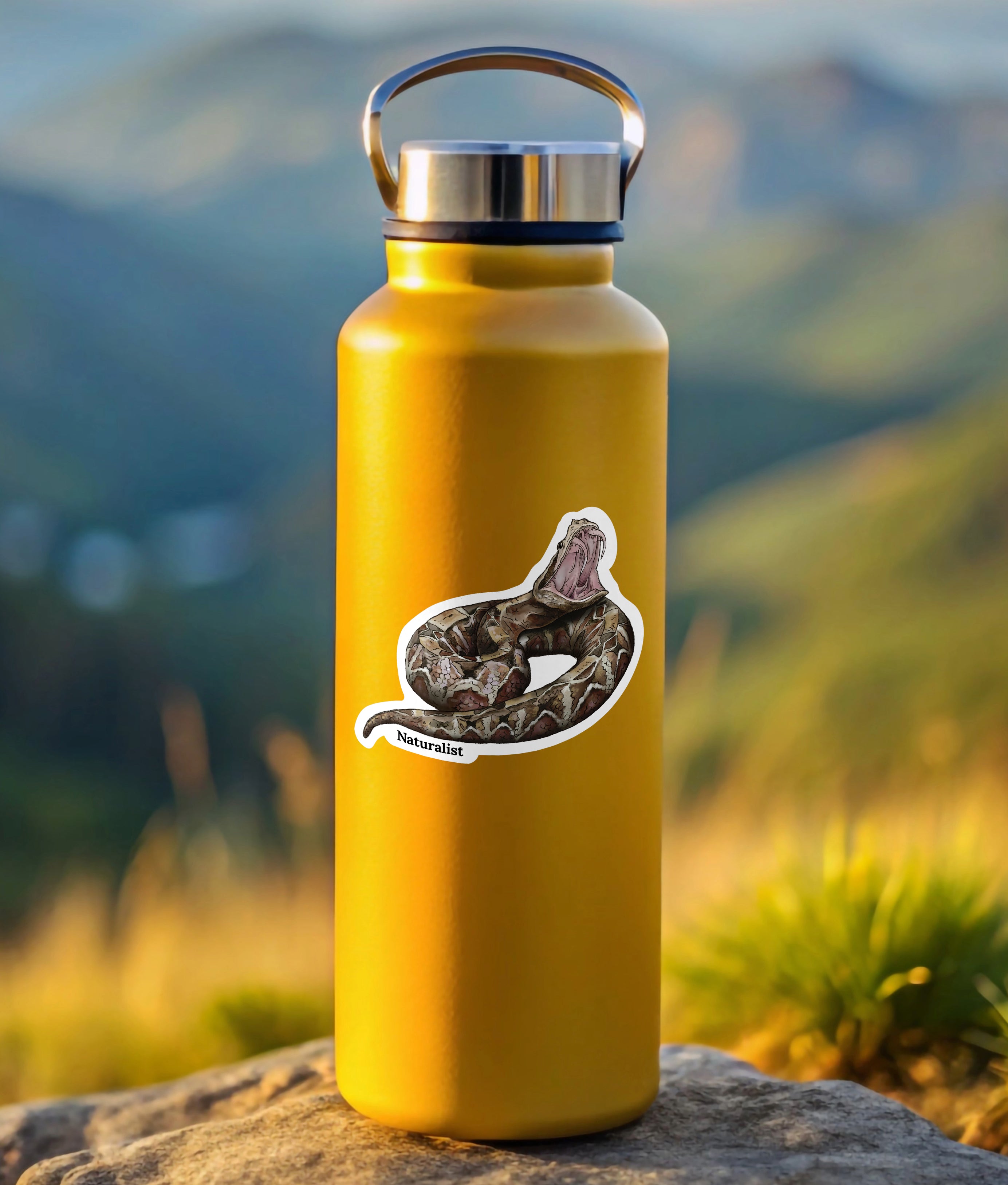 Yellow water bottle with a gaboon viper  sticker on a rock with a mountainous background