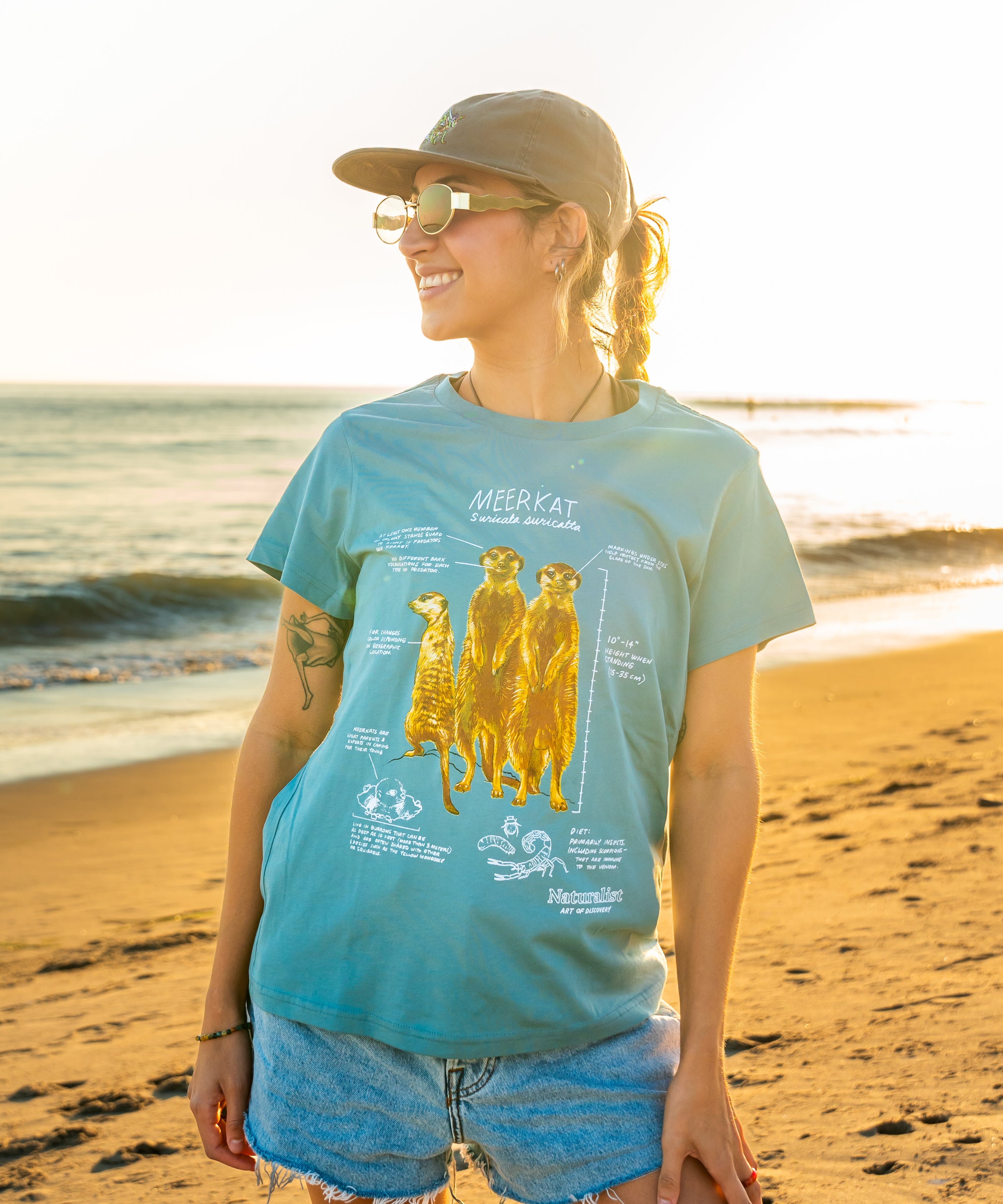 Woman wearing a light blue t-shirt with a meerkat illustration on a beach