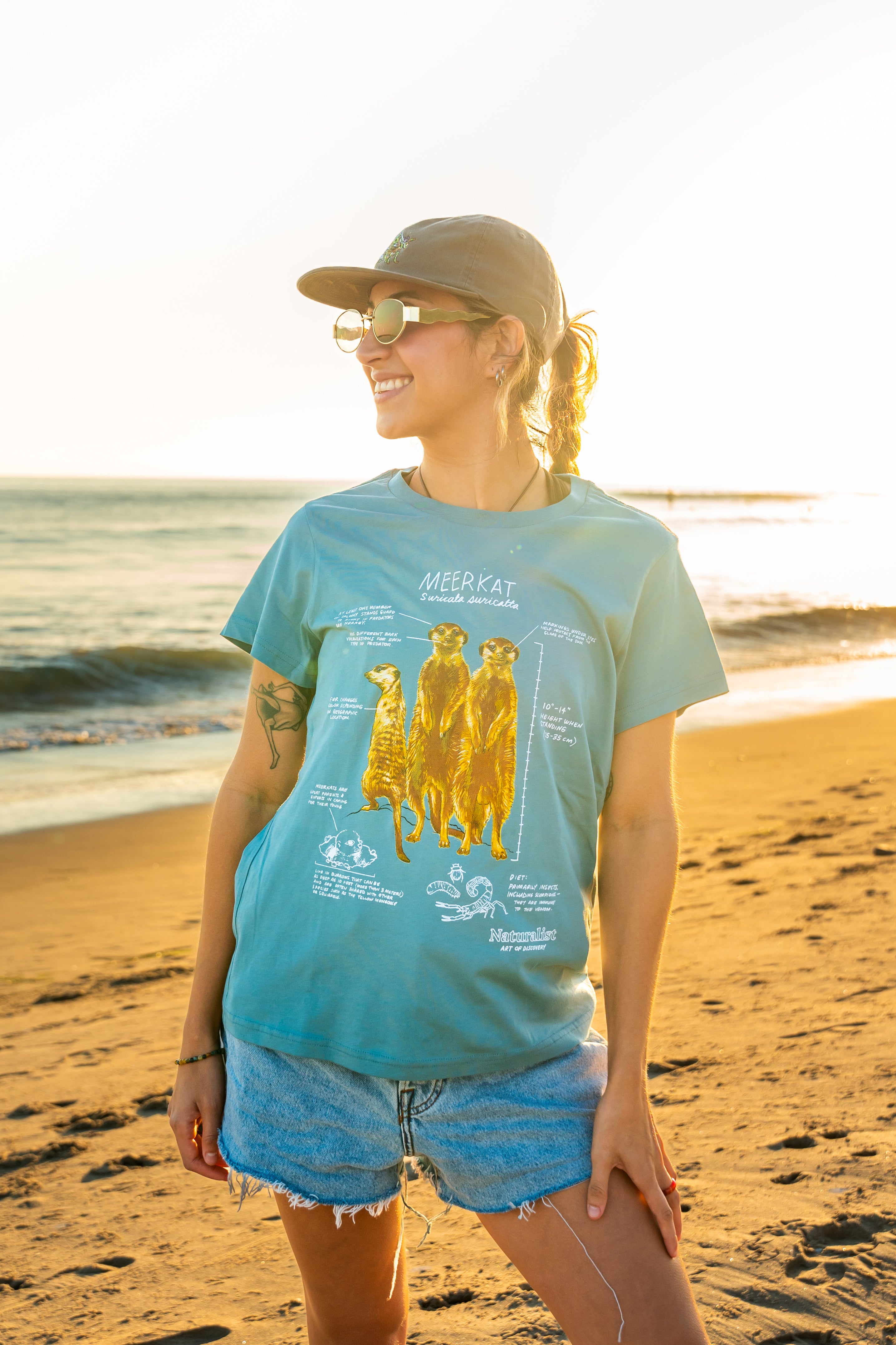 Woman wearing a light blue t-shirt with a meerkat illustration on a beach