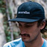 Person wearing a navy cap with 'Naturalist' text, outdoors.