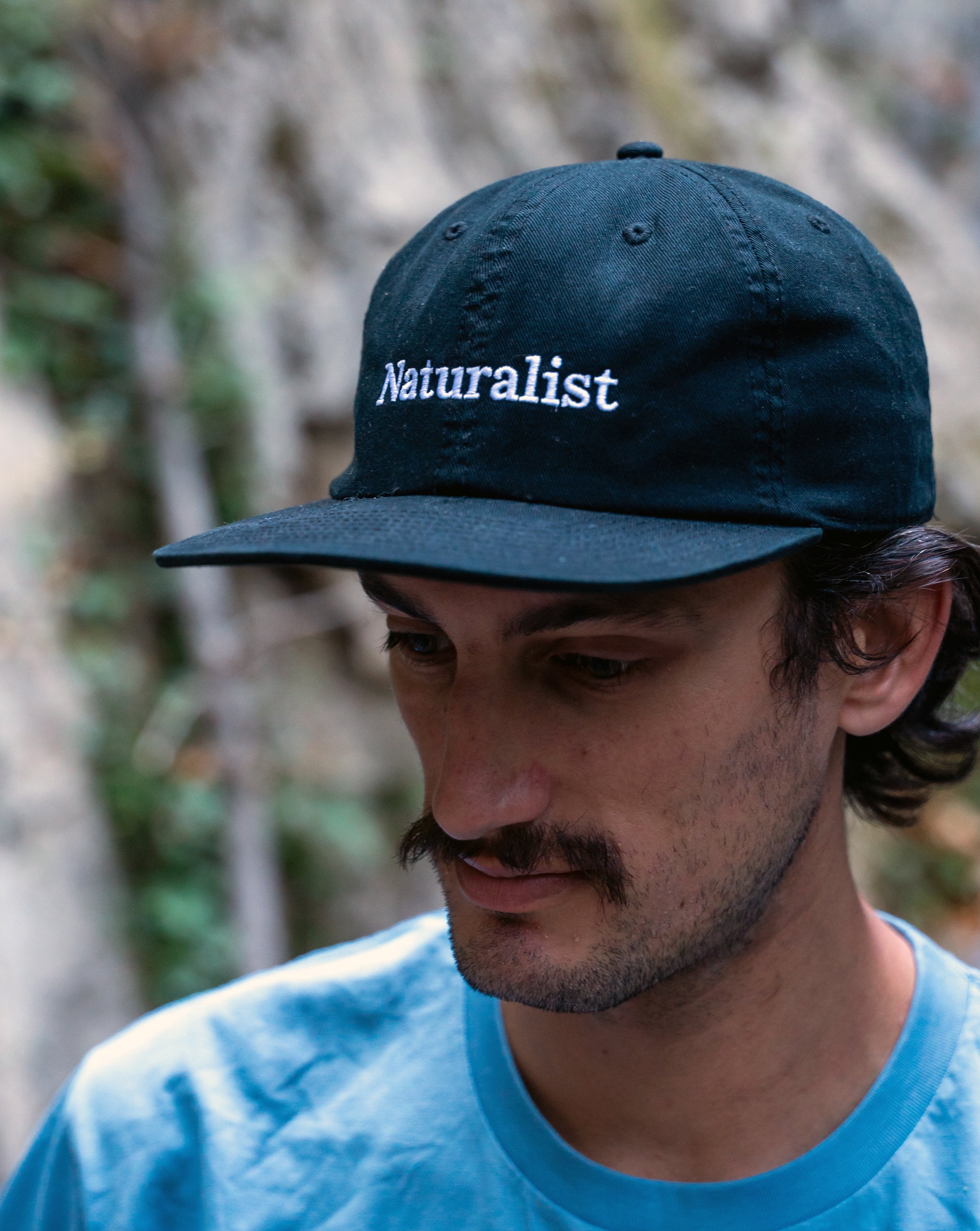 Person wearing a navy cap with 'Naturalist' text, outdoors.