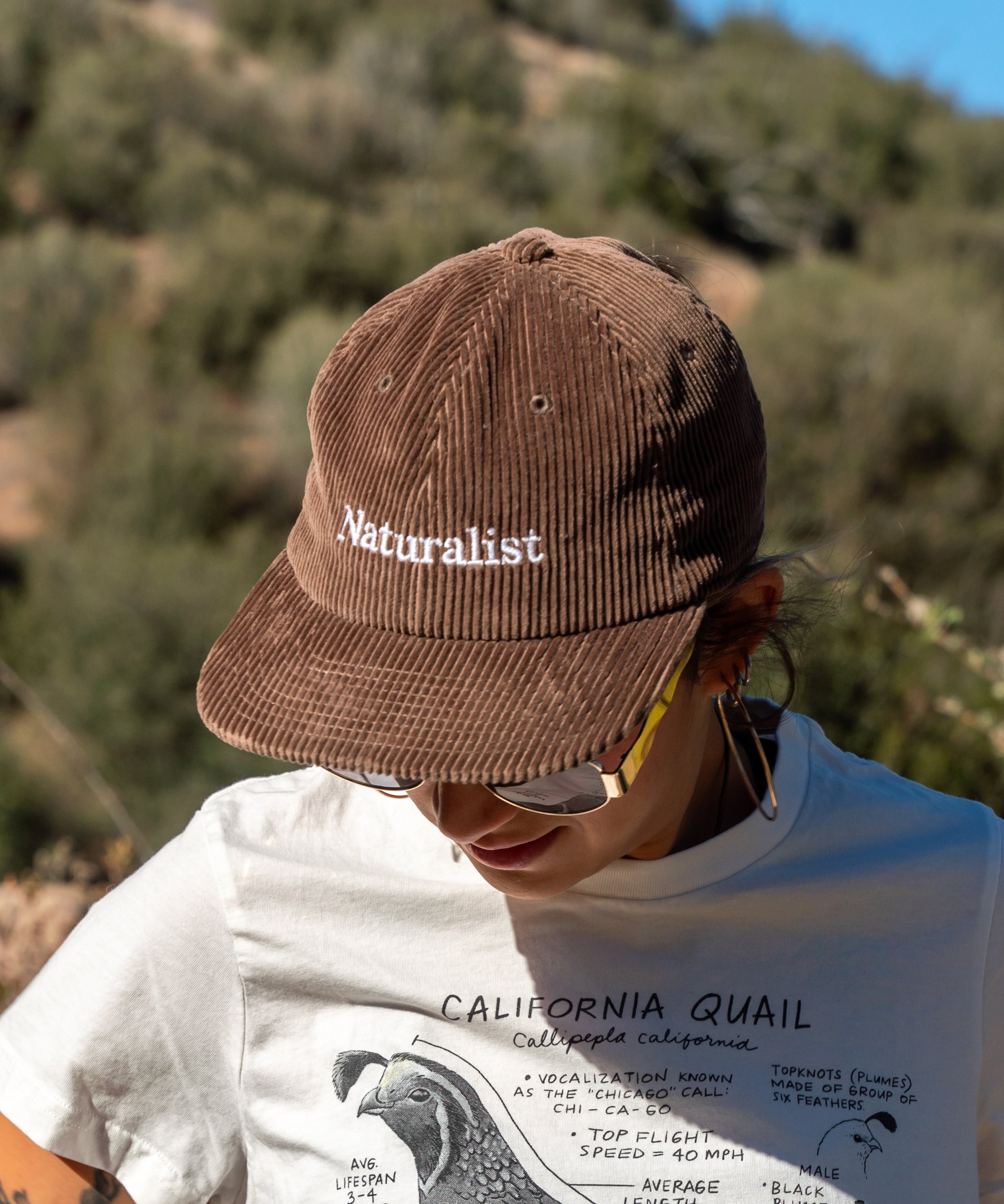 Person wearing a brown 'Naturalist' cap with a blurred natural background