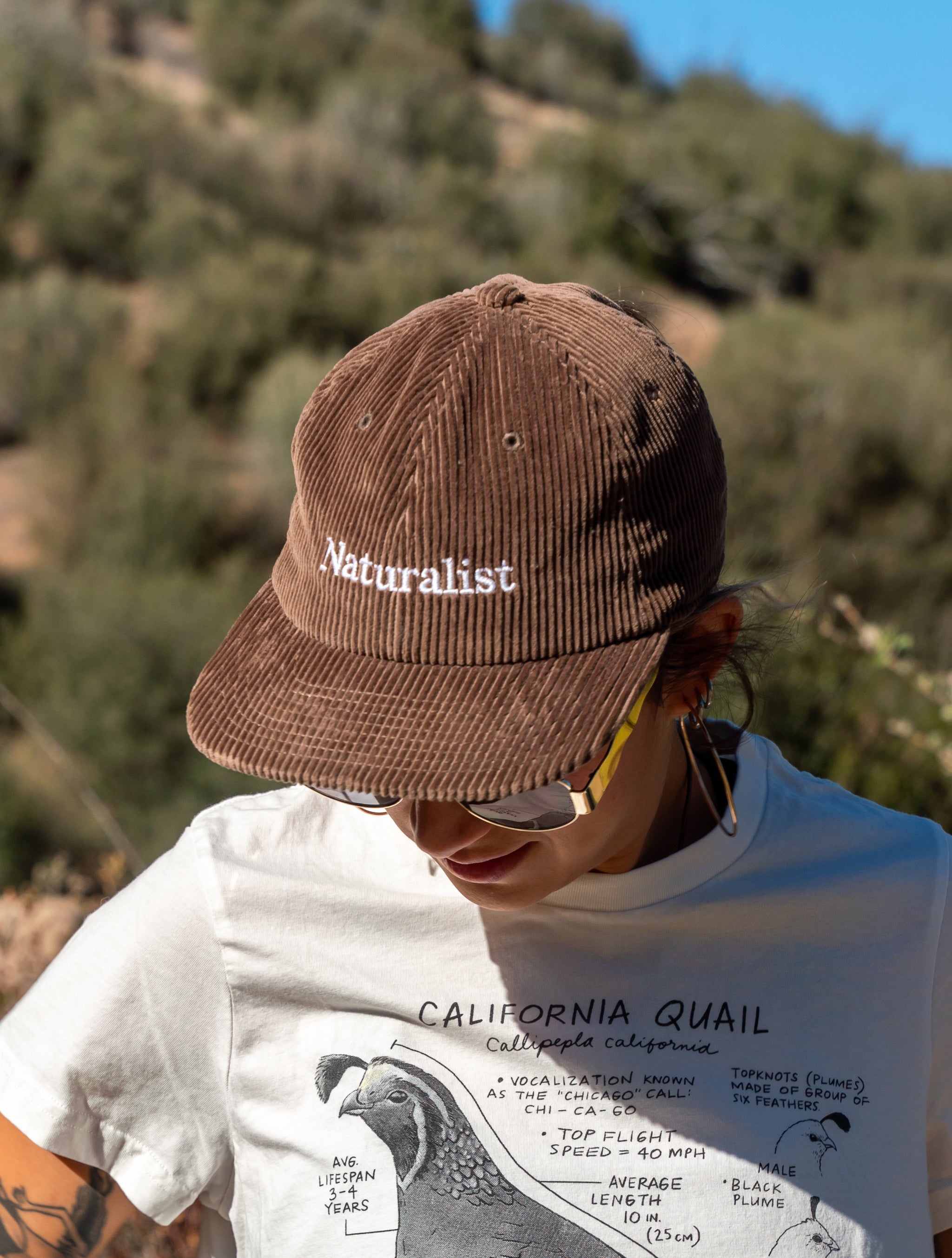 Person wearing a brown 'Naturalist' cap with a blurred natural background