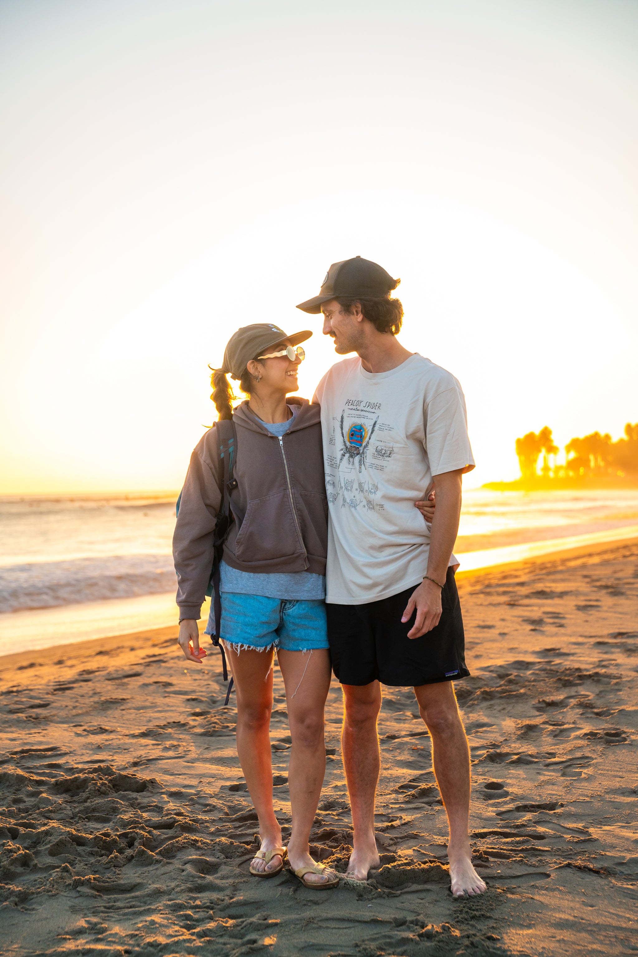 Two people standing on a beach at sunset
