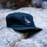 Navy blue cap with a quail design on a stone surface