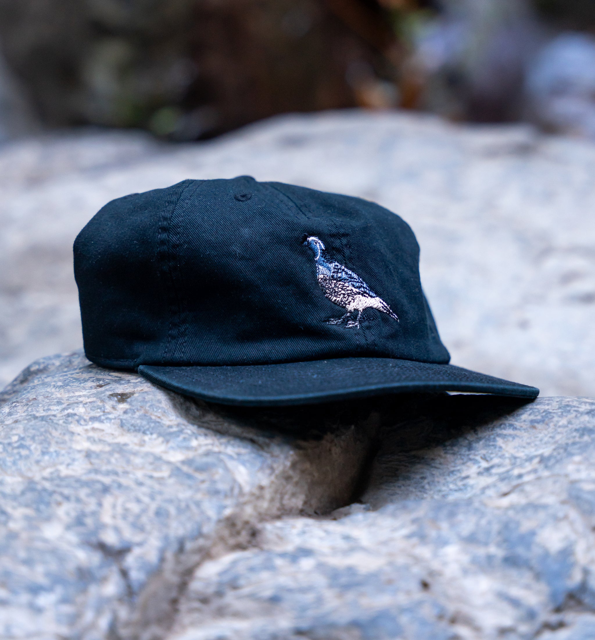 Navy blue cap with a quail design on a stone surface