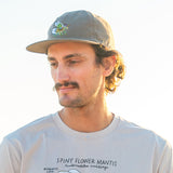 Man wearing a cap and t-shirt with text an illustration of a spiny flower mantis, standing outdoors.
