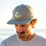 Man wearing a cap with a spiny flower mantis standing by the ocean.