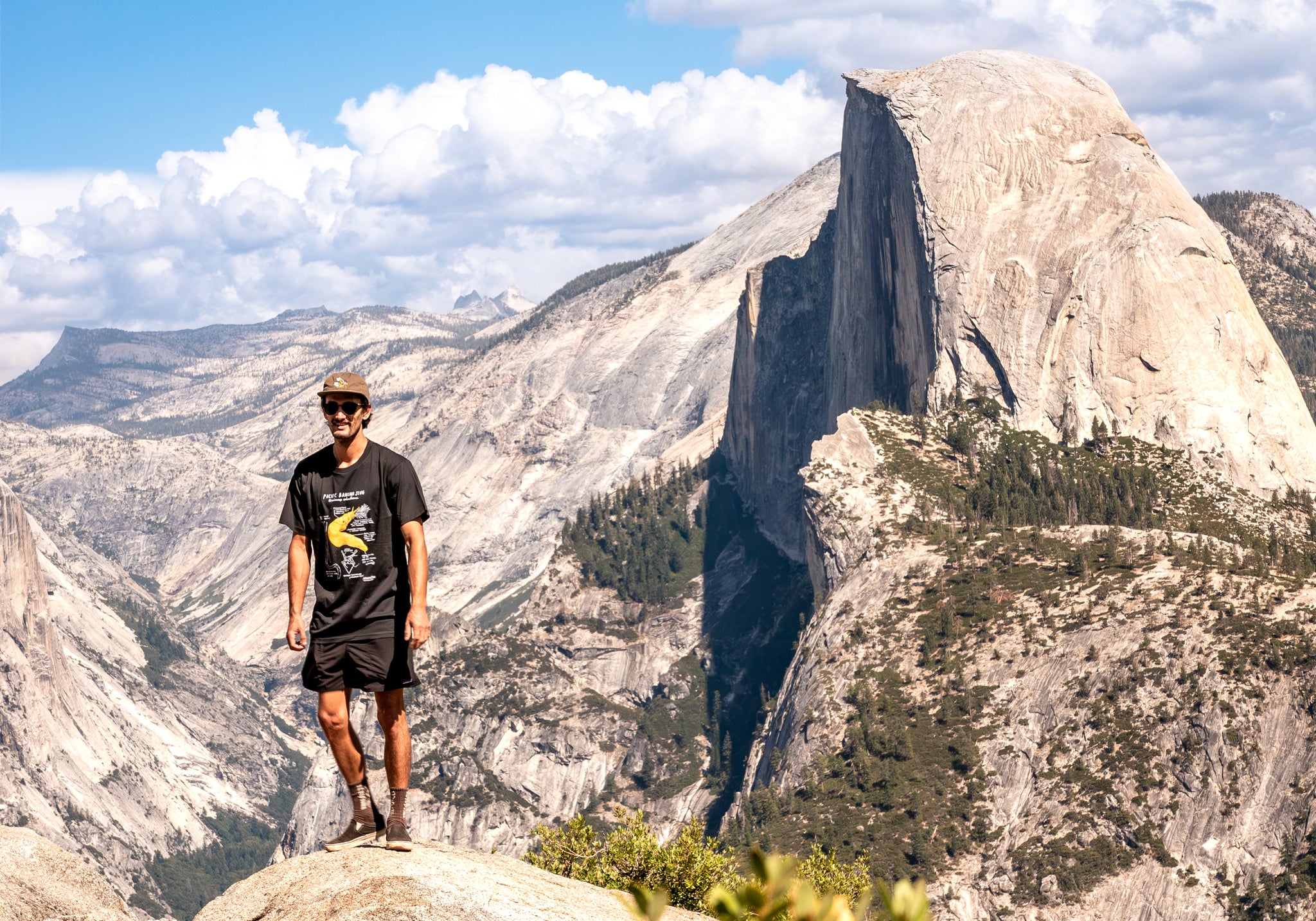 Person standing on a rock with a mountainous landscape and Half Dome in the background